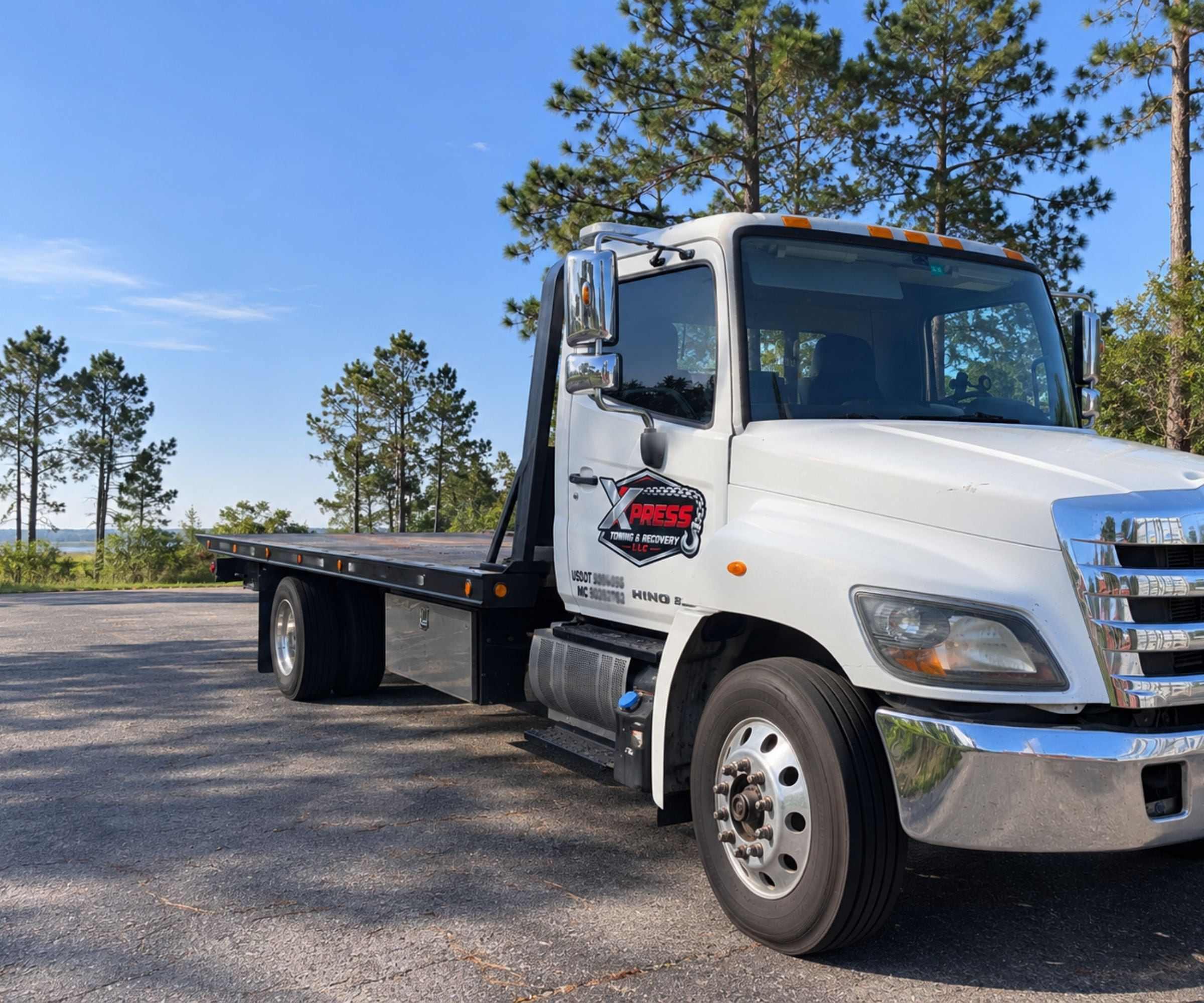 Xpress Towing white Hino flatbed carrier with empty deck, parked three-quarter front on the lot in Mobile